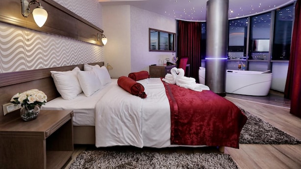 Una moderna camera d'albergo con un letto grande, un'area salotto, vista sulla città e bagno con vasca.