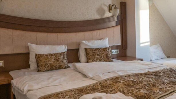 Hotellihuone, jossa on suuri sänky, kaksi tyynyä, yöpöytä, seinään kiinnitetty valaisin ja ikkuna.