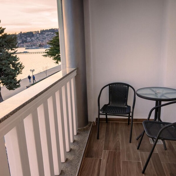 A balcony with a view of a waterfront, two wicker chairs, and a small round table. - City Palace Hotel (Ohrid)