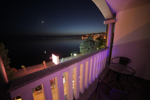 A balcony with a view of a calm lake at night, a chair, and a table. - City Palace Hotel (Ohrid)