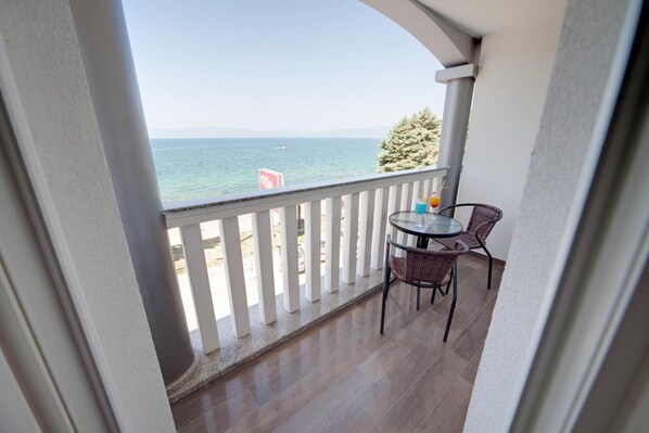 A balcony with a view of the sea, a table with chairs, and a sign in the background. - City Palace Hotel (Ohrid)