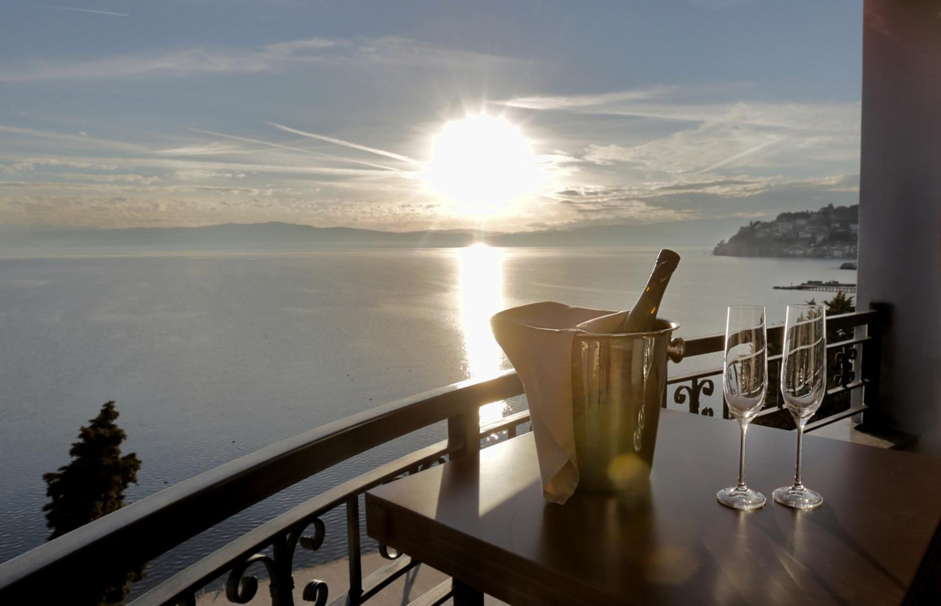 Ein Tisch mit einer Flasche und Gläsern, mit Blick auf ein Gewässer bei Sonnenuntergang.