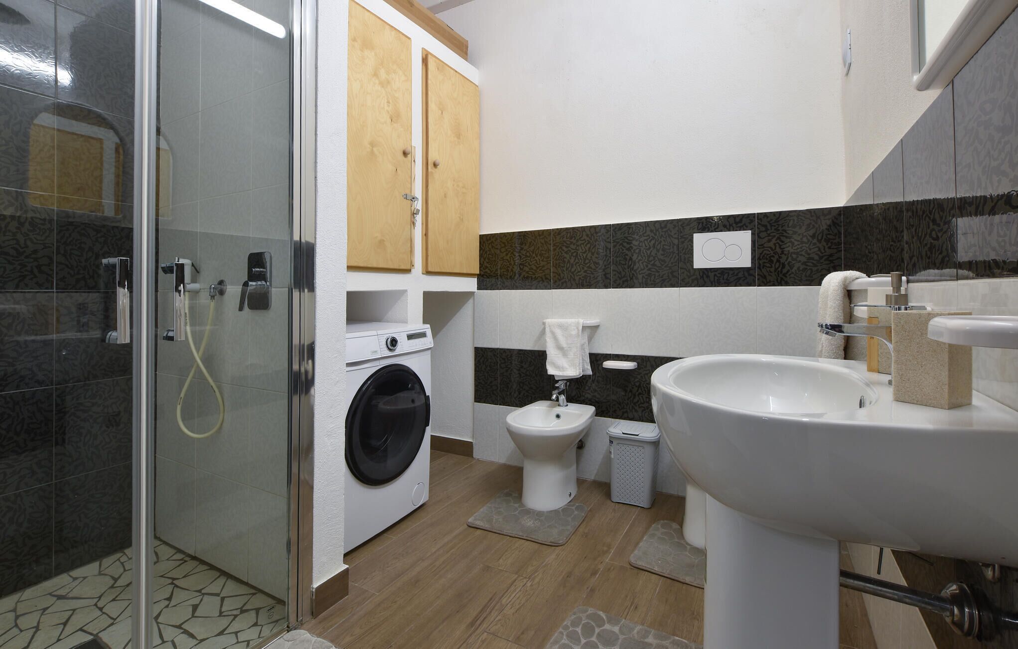 Een badkamer met een douchecabine van glas, een wasmachine, een toilet en een wastafel.