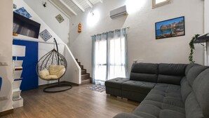 A living room with a sofa, a hanging chair, a staircase, and a painting on the wall. - 2 bedroom lovely home in Castellammare del Golf (Castellammare del Golf)