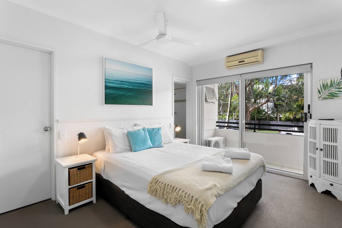 A bedroom with a bed, nightstand, lamp, and a view of the outdoors.