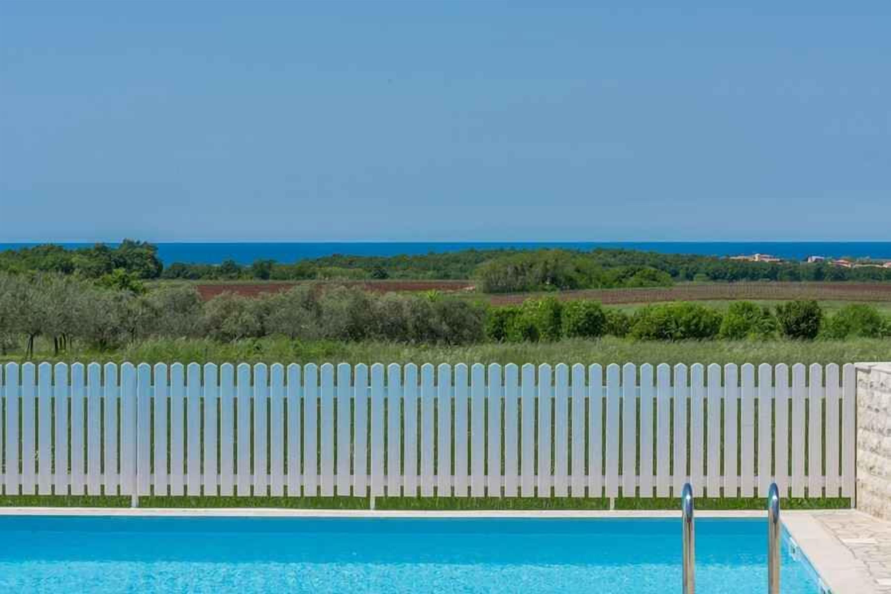 A swimming pool with a white picket fence and a view of the sea.