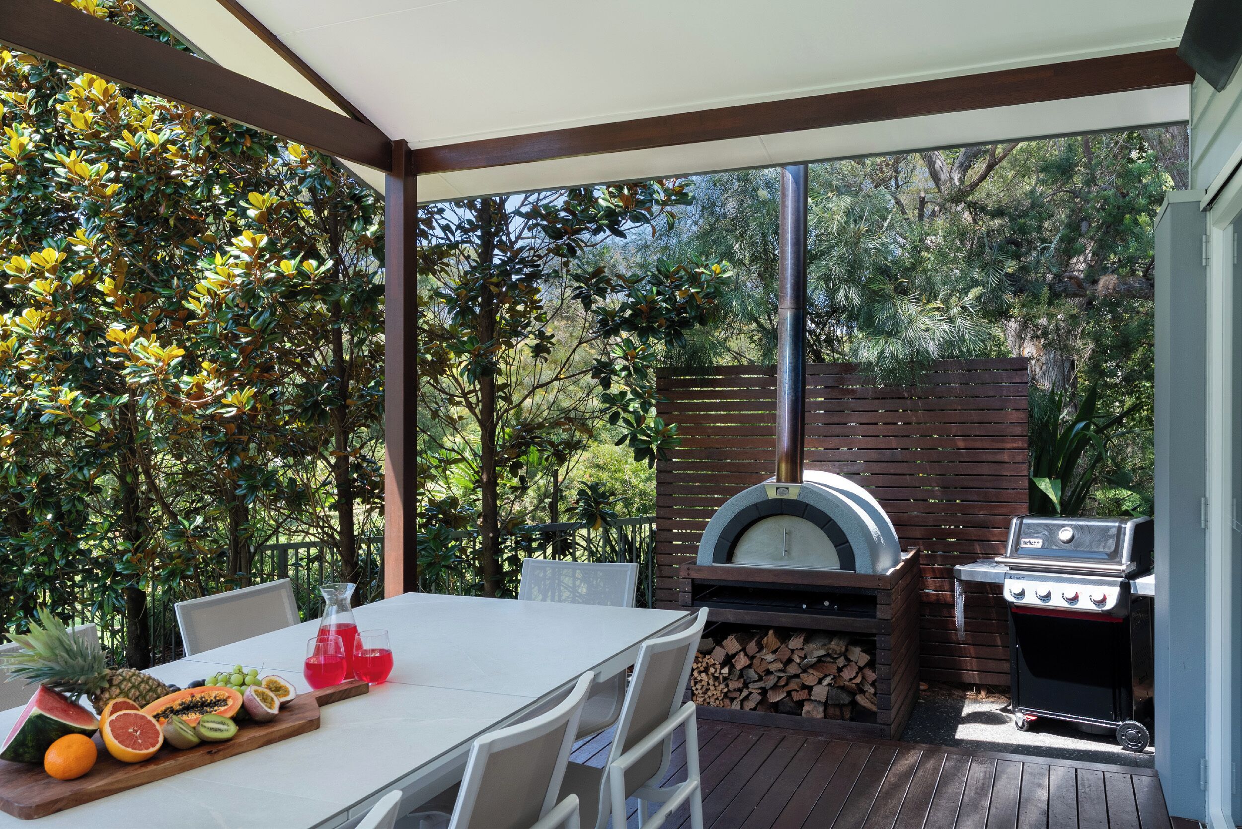 Un patio exterior con una mesa lista para comer, una parrilla y un horno para pizza.