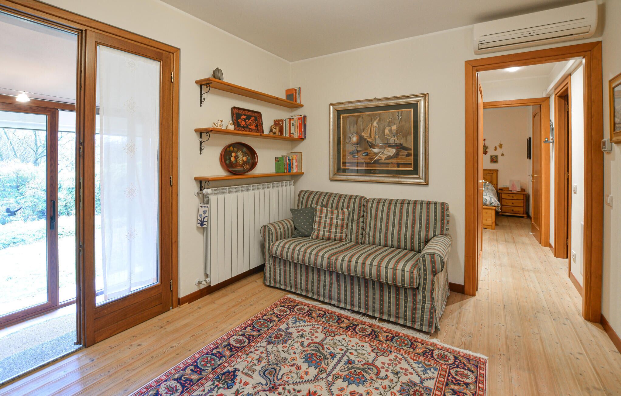 A room with a sofa, a patterned rug, a radiator, and a painting on the wall.