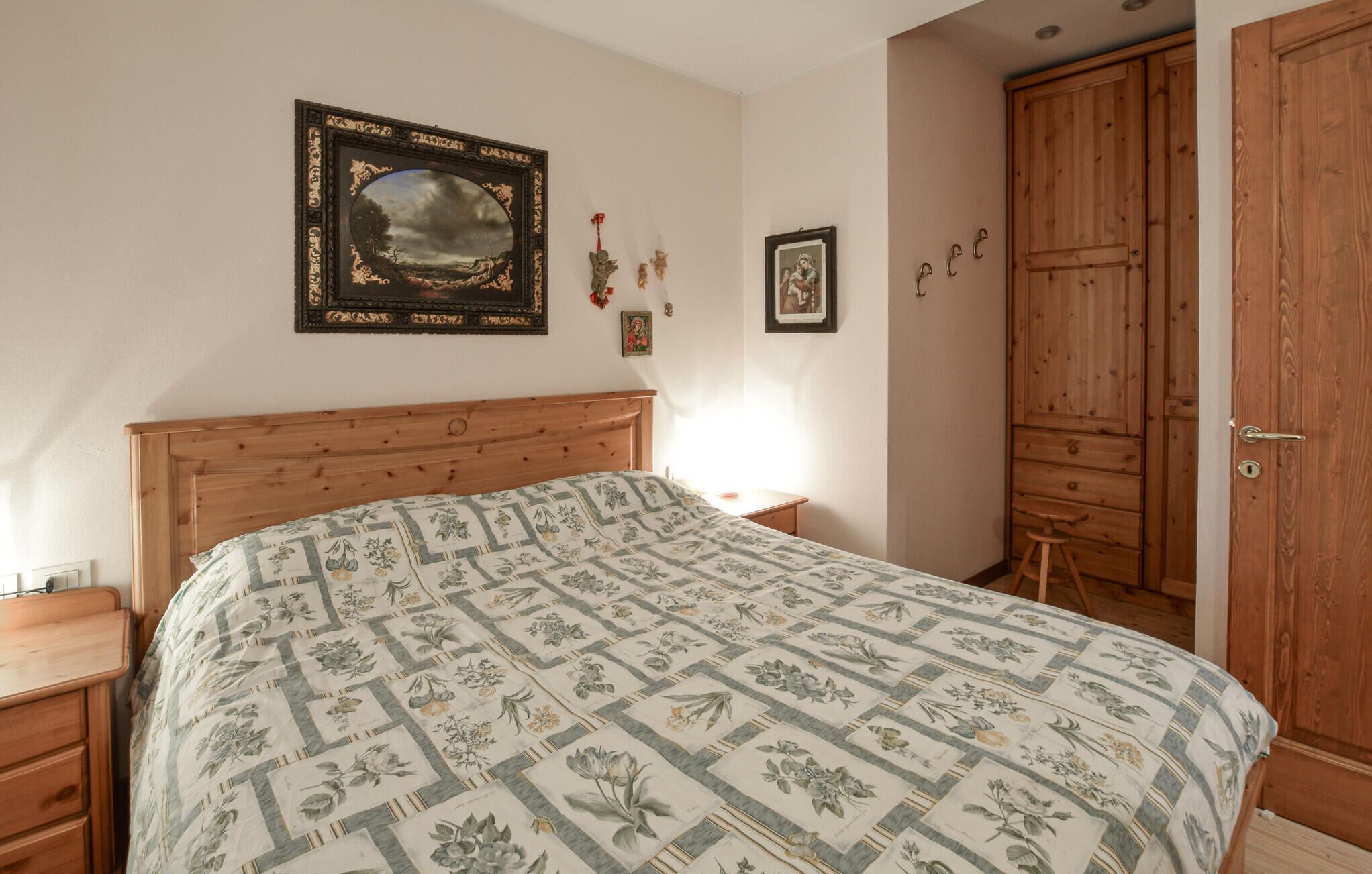 A bedroom with a wooden bed, a nightstand, a wooden wardrobe, and a framed landscape painting on the wall.
