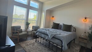 A bedroom with a bed, a chair, a TV, a ceiling fan, and large windows. - Riverfront Property with Direct Access & Private Pier (Robstown)