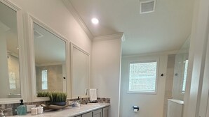 A modern bathroom with a large mirror, a sink, and a toilet. There are two rugs on the floor, and a window with blinds. - Riverfront Property with Direct Access & Private Pier (Robstown)