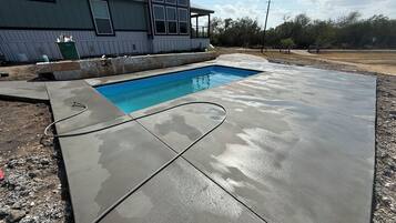 A swimming pool with a concrete deck, a house in the background, and a clear sky.