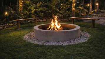 A fire pit surrounded by a grassy area, with string lights and trees in the background.