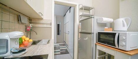 A compact kitchen with a coffee maker, microwave, and a bowl of fruit on the counter.
