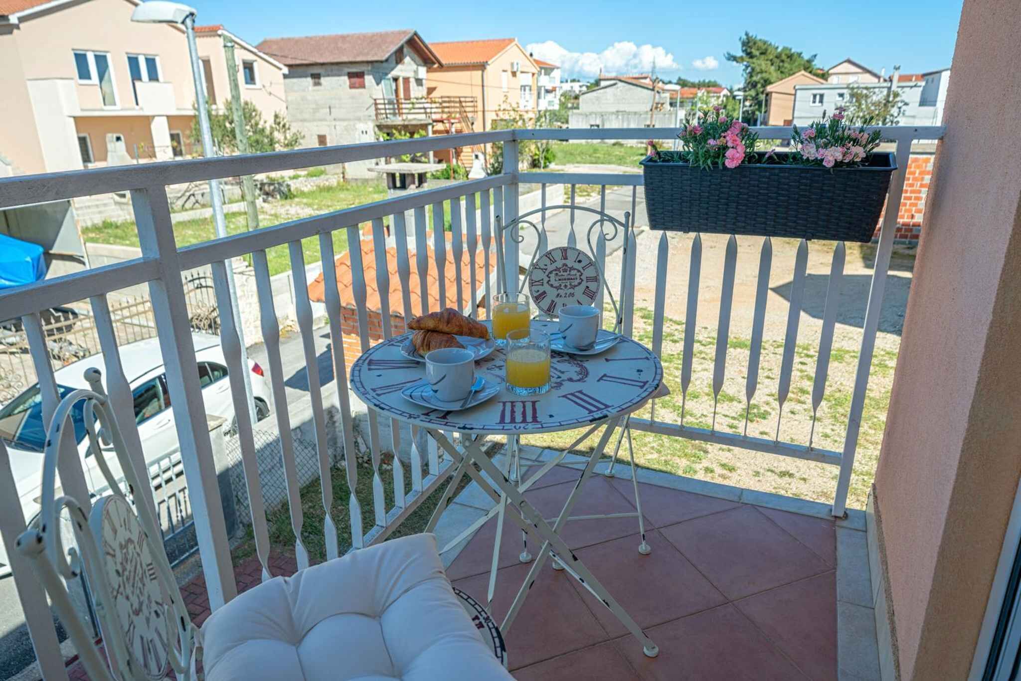 Un balcon avec une table préparée pour le petit-déjeuner, une chaise et un pot de fleurs suspendu.