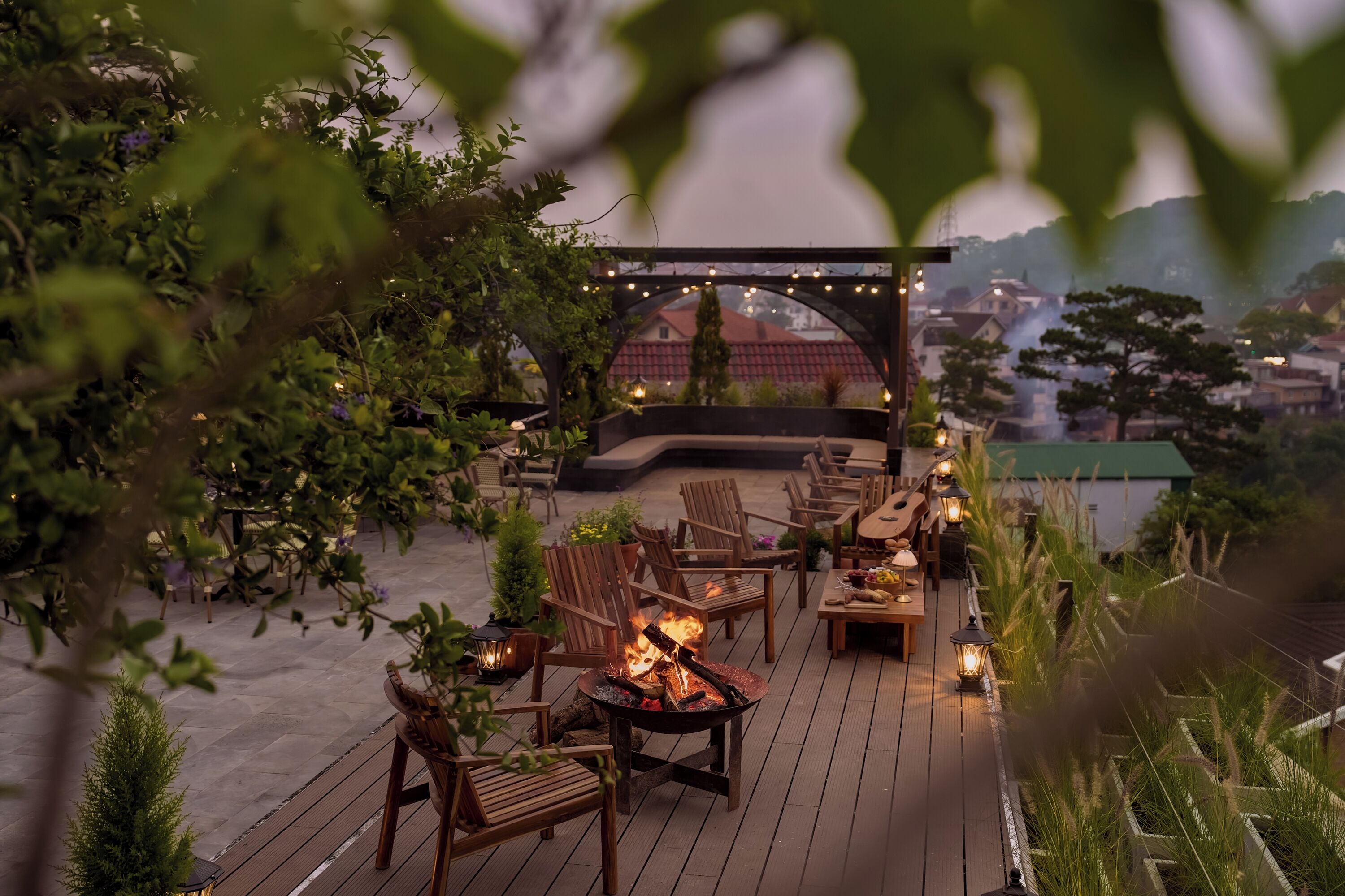 A deck with chairs and a fire pit, surrounded by greenery and string lights.