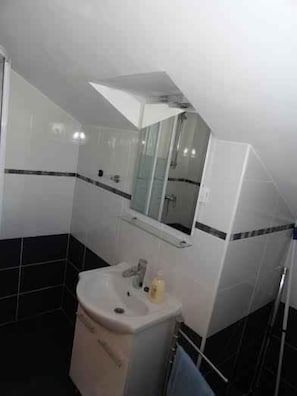 Casa de banho com lavatório branco, espelho e chuveiro.