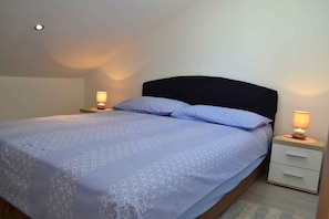 Uma cama de solteiro com cabeceira, duas mesas de cabeceira com luminárias e um pequeno conjunto de gavetas.