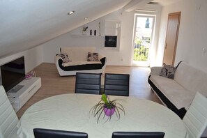 A modern living room with a white sofa, black chairs, a dining table with a purple plant, and a TV on a stand. - Holiday Apartment Zorana 4+2 (Vodice)