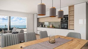 A modern kitchen with white cabinets, a wooden dining table, and a view of the sea. - Holiday Apartment Sabbia 6+0 (Srima)