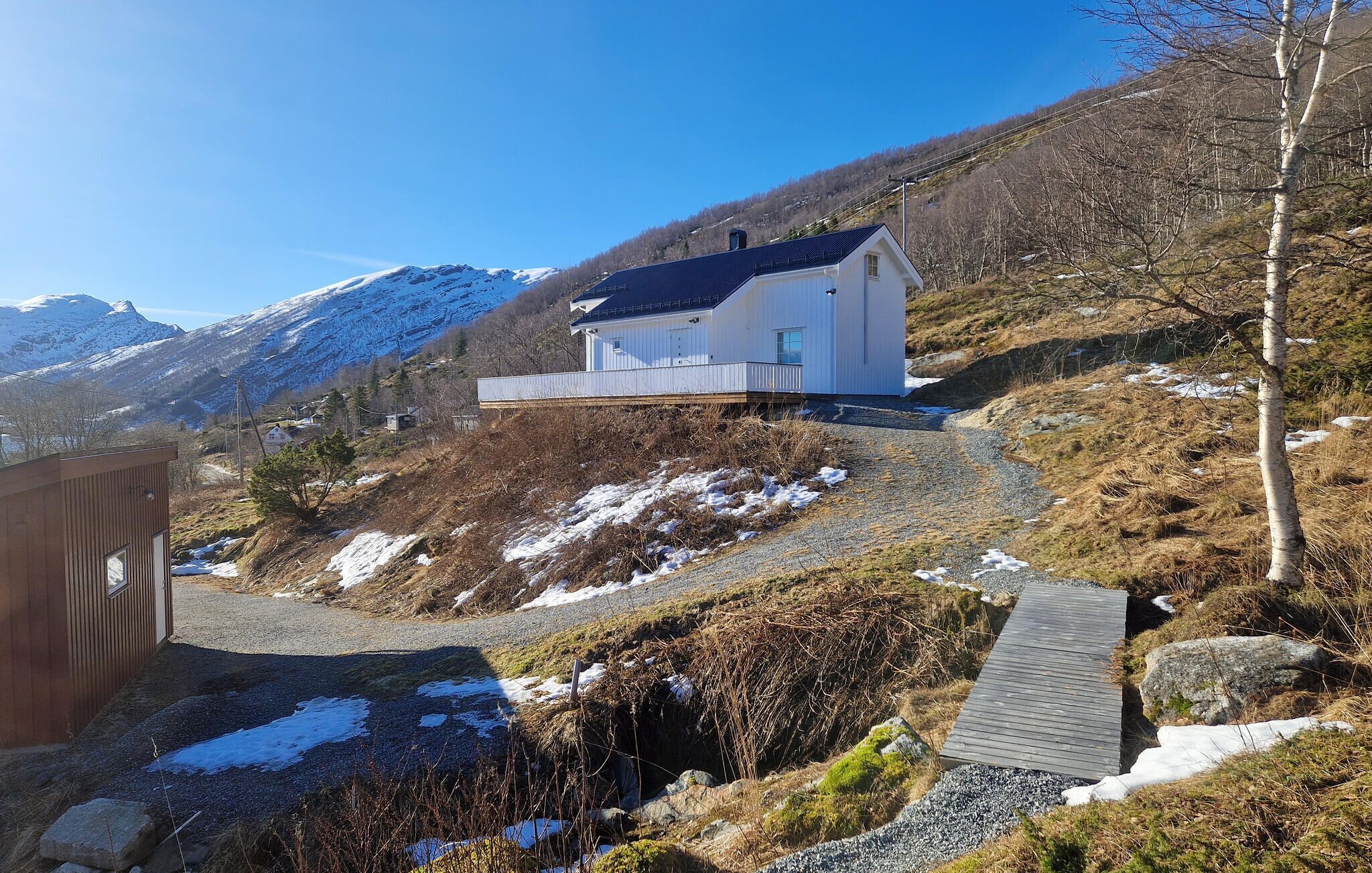A modern house with a sloped roof, surrounded by a mountainous landscape with snow patches.