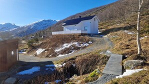 Een modern huis met een schuin dak, gelegen in een bergachtig landschap met sneeuwvlekken.