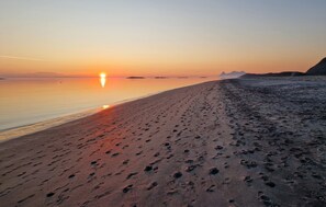 Una playa con huellas que conducen al agua, un atardecer de fondo y montañas distantes.