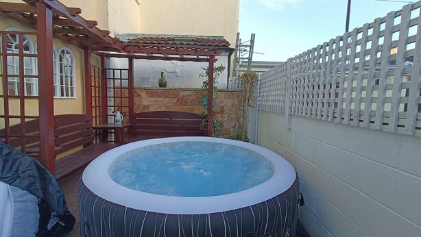 A hot tub in a backyard with a pergola, wooden bench, and a white fence.