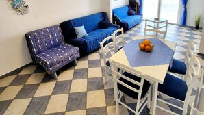 Un salon moderne avec un sol à carreaux, un canapé bleu, une table à manger avec des chaises et un balcon agrémenté de rideaux bleus.