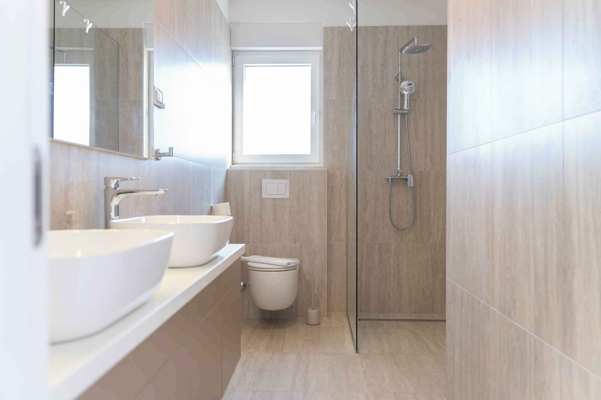 A modern bathroom with two sinks, a toilet, a shower, and a window.