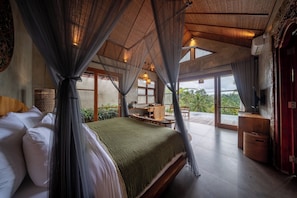 A bedroom with a large bed, a desk, and a view of the outdoors.