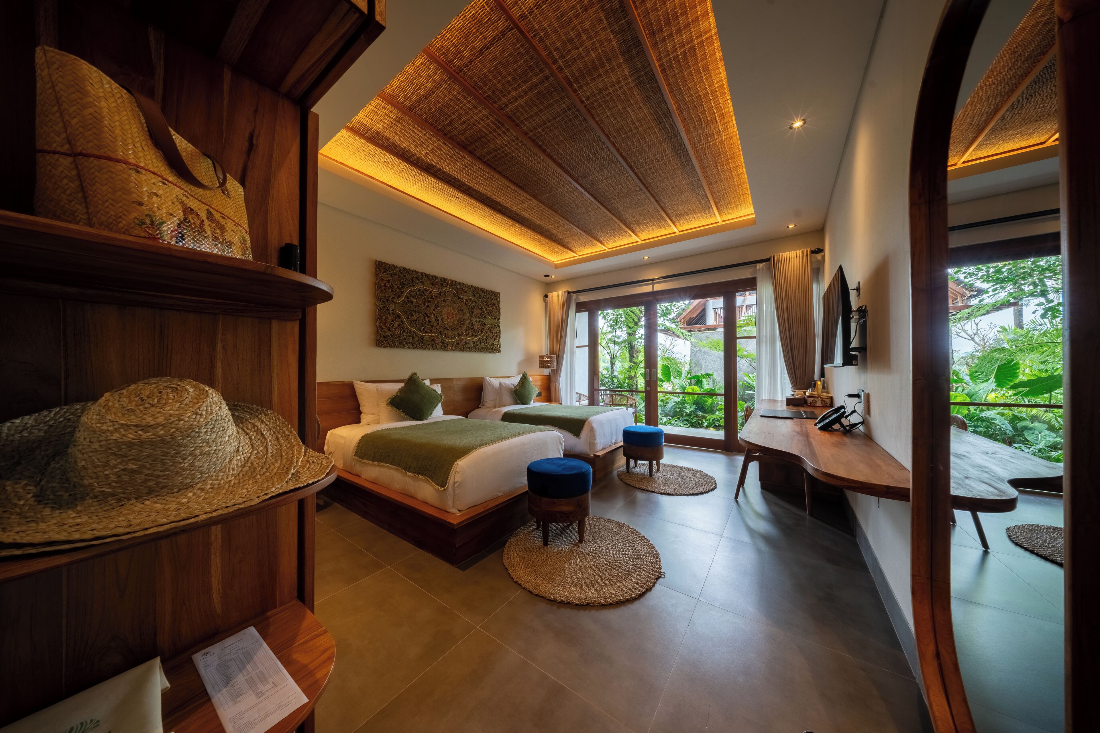 A room with a bed, two bedside tables, a desk, and a view of greenery outside.