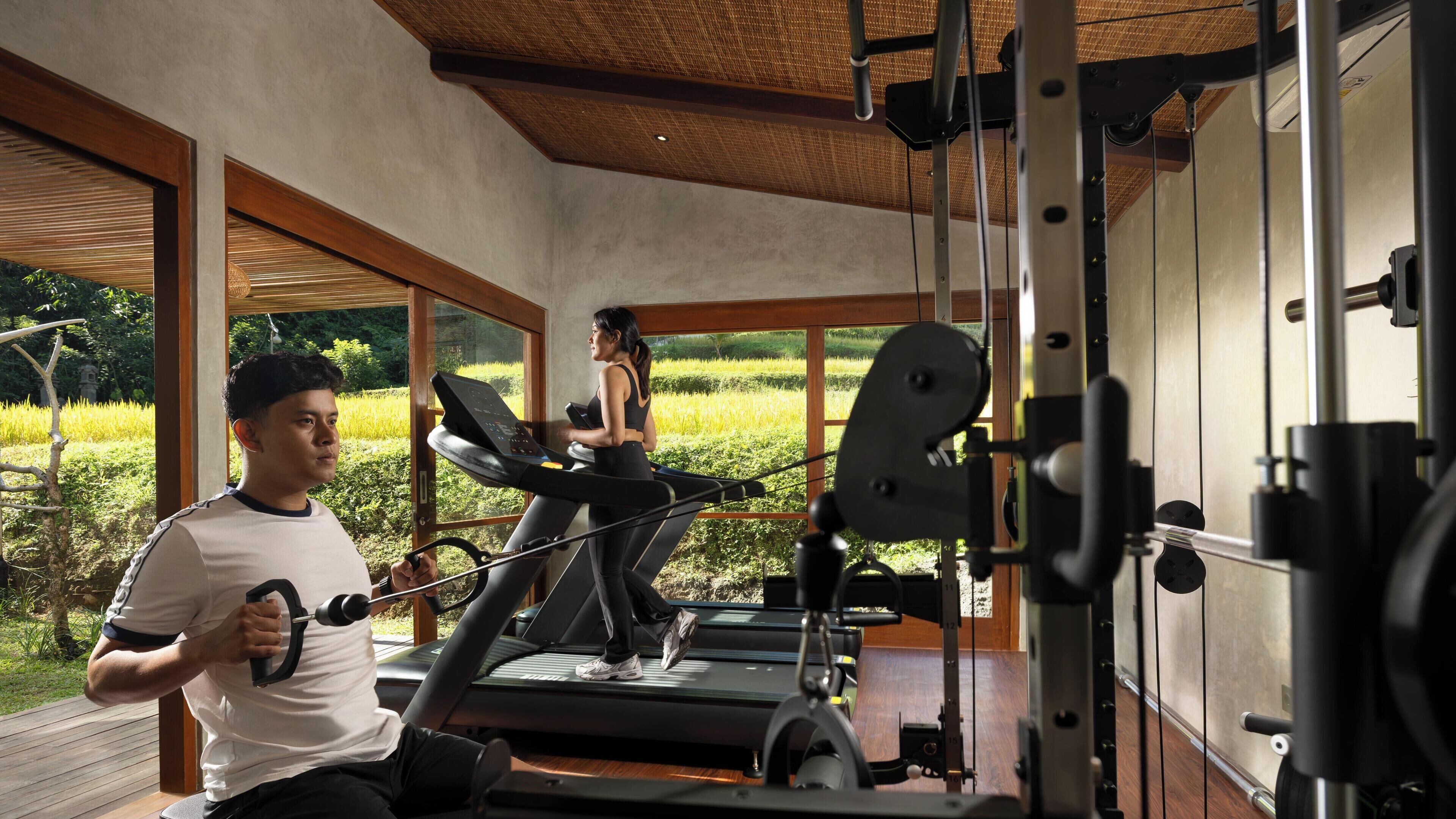 A gym with treadmills, a weight machine, and large windows offering a view of a green landscape.