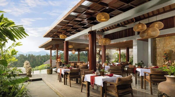 An outdoor restaurant with wooden tables and chairs, surrounded by greenery and a view of the mountains. - ULU Valley Retreat (Sebatu)