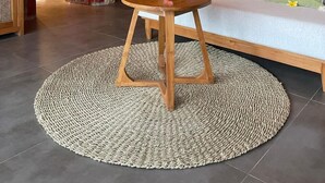 Una stanza con un tavolo rotondo in legno, un divano con cuscini, uno specchio decorativo e un tappeto tessuto.