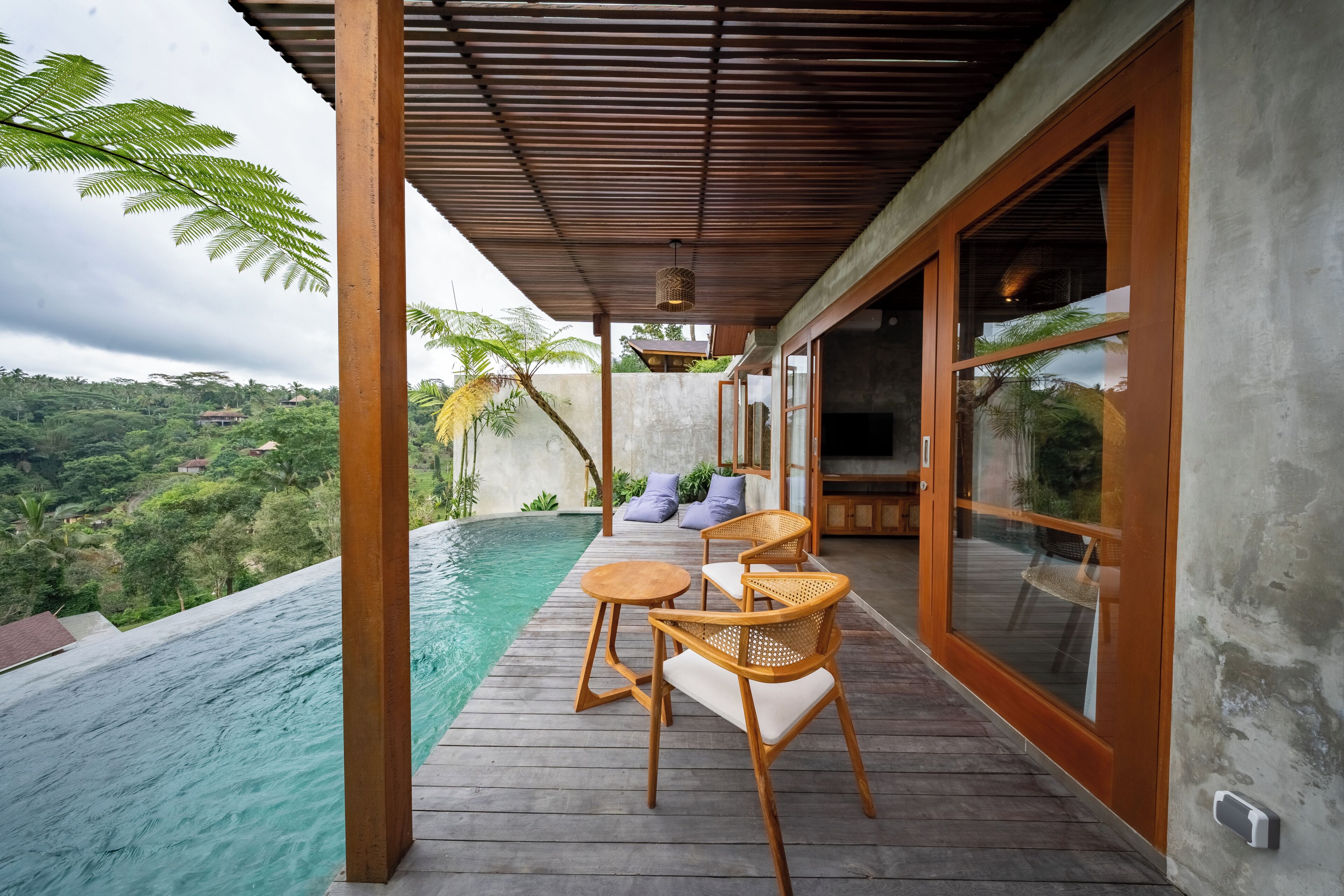 A wooden deck with a pool, wicker chairs, and a view of a lush landscape.