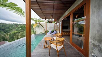 A wooden deck with a pool, wicker chairs, and a view of a lush landscape.