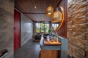 Une salle de bain moderne avec un mur en pierre, une porte rouge, une grande fenêtre, un lavabo et un comptoir en bois.