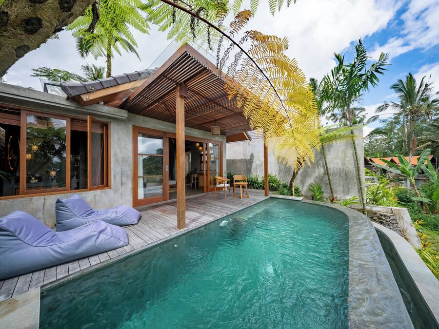 Una casa moderna con piscina, terraza de madera y exuberante vegetación.