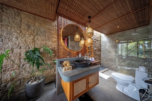A bathroom with a stone wall, a large mirror, a sink with a bowl, a toilet, and a shower area.
