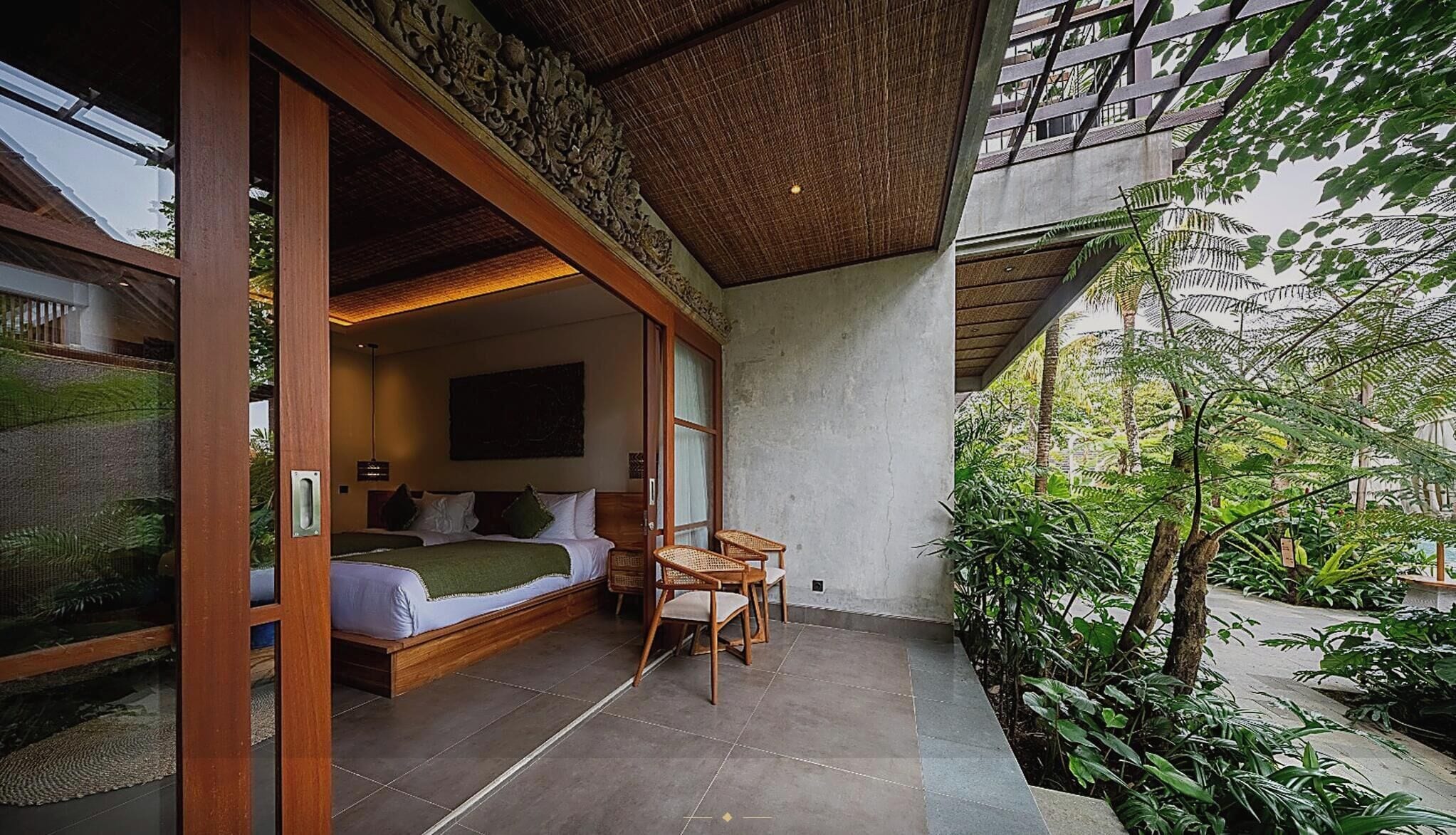 A room with a bed, a table, and chairs, a large window, and a view of greenery outside.