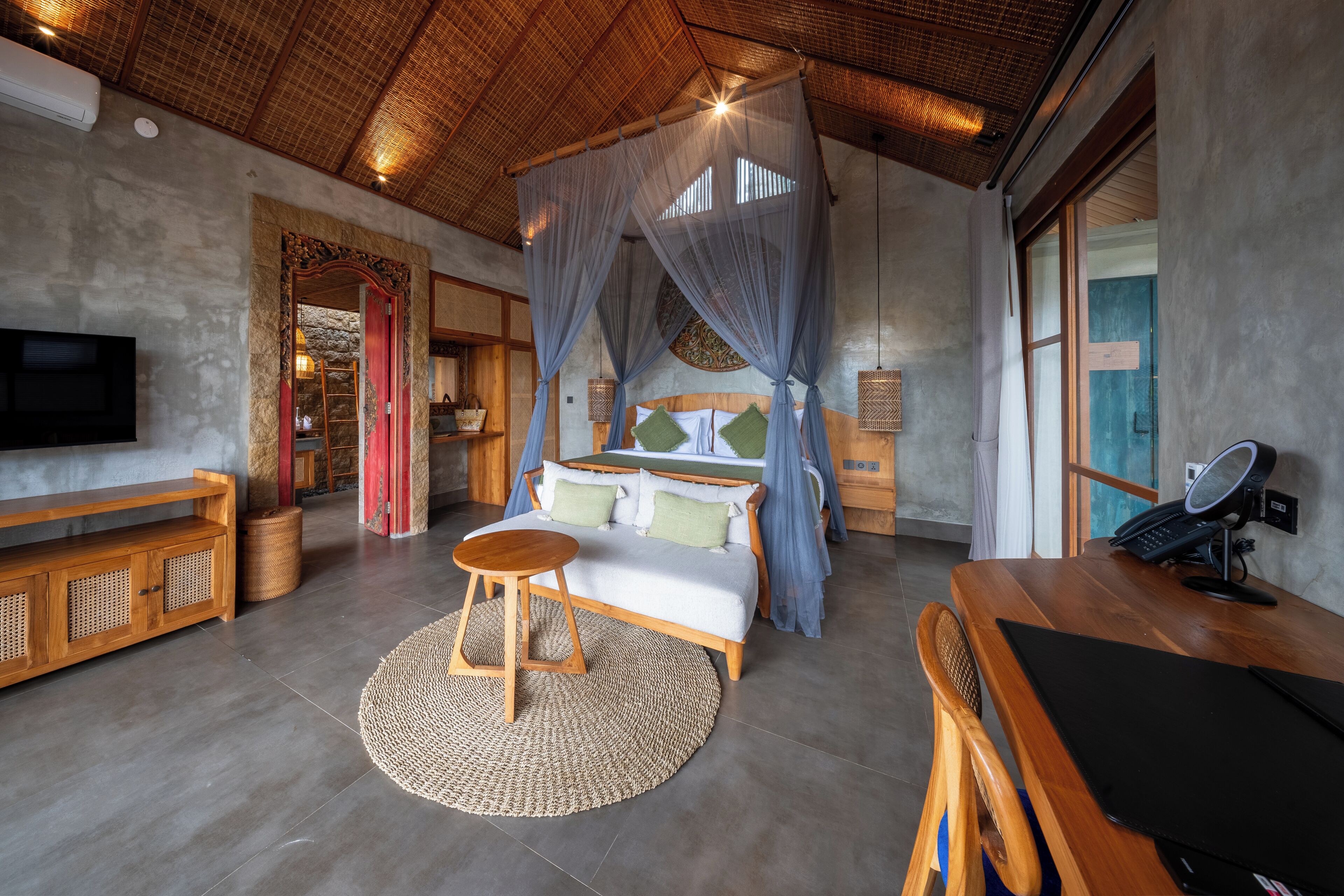 A room with a bed, a desk, a television, and a woven rug.
