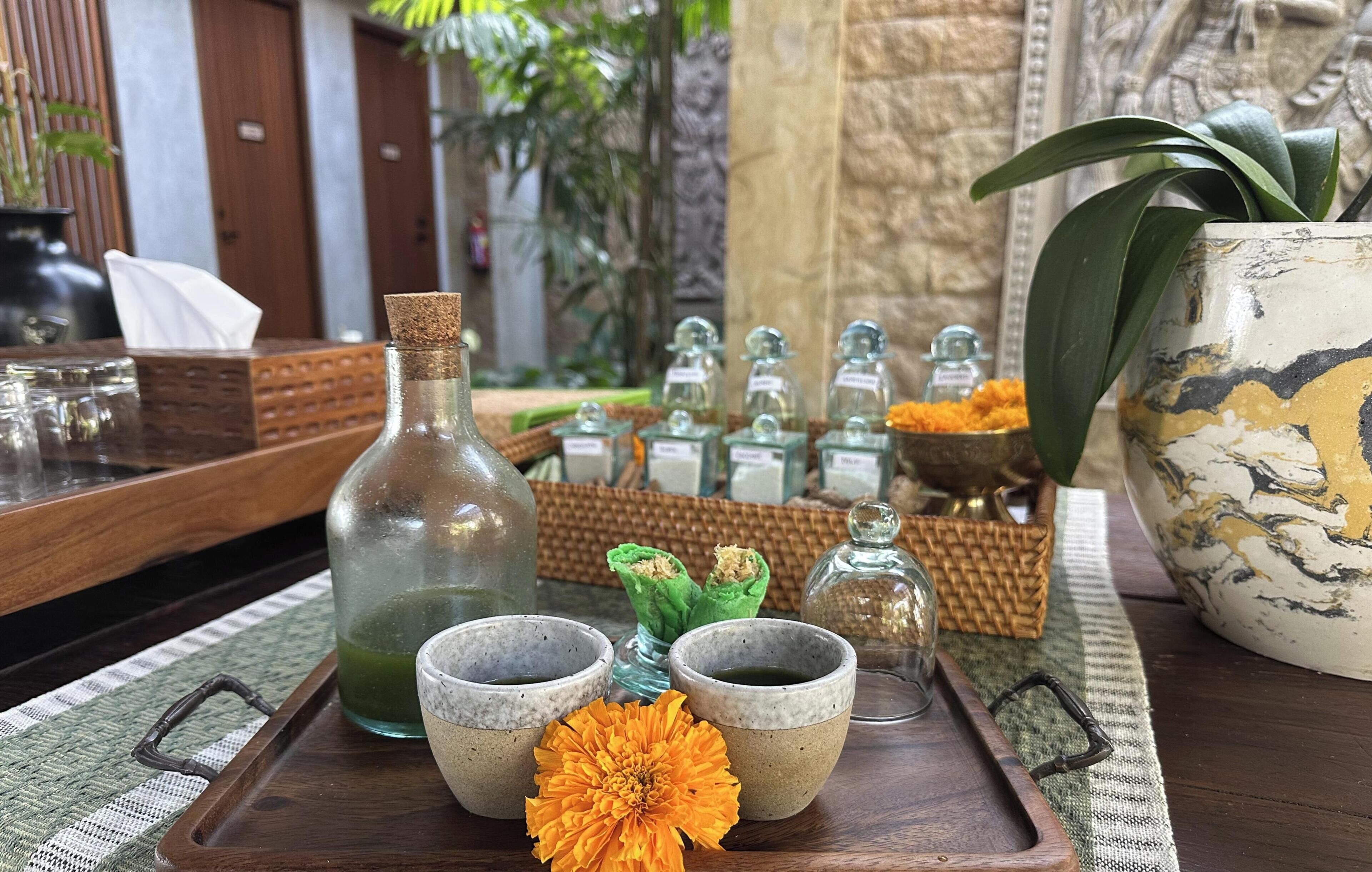 A tray with two ceramic cups, a bottle, and a flower on a wooden table.