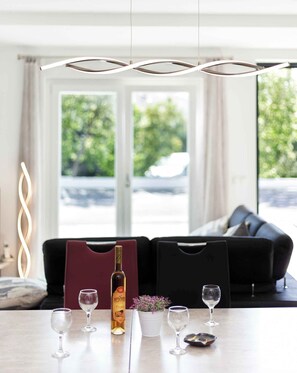 Una sala de estar moderna con un sofá, una mesa con copas de vino y una botella, y un elemento de iluminación decorativo.