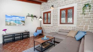 A living room with a stone wall, a sofa, a chair, a coffee table, and a painting of a coastal landscape. - Villa VILLA MARIJANA 6+0 (Srima)