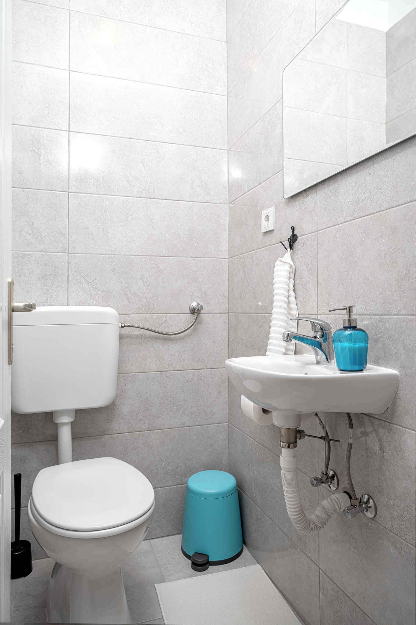 Un baño con inodoro, lavamanos y un cubo de basura azul.