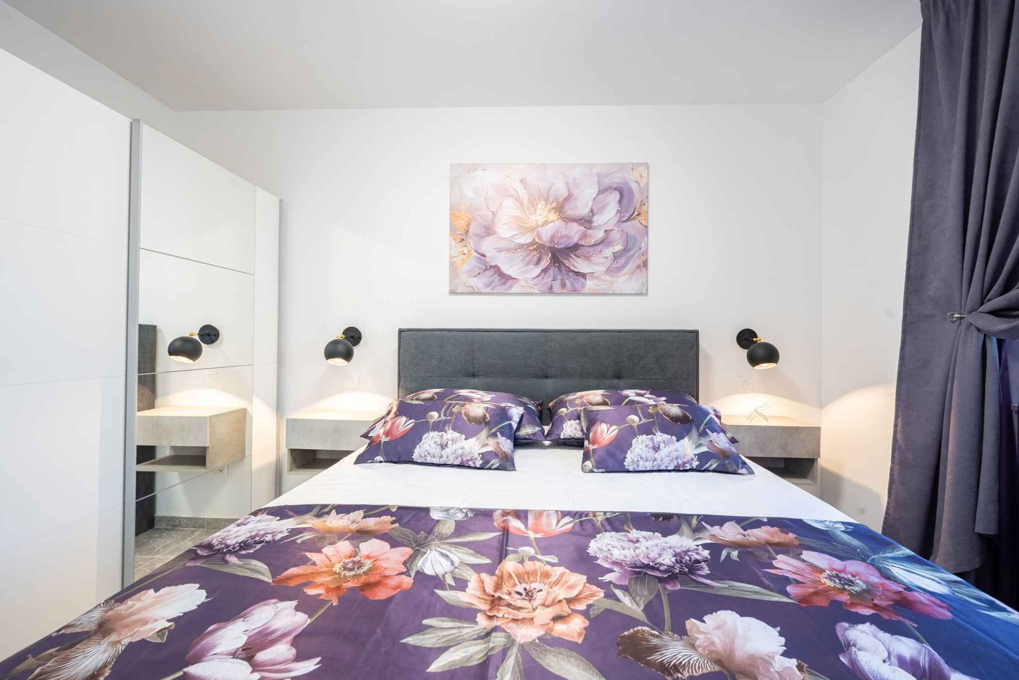 A bedroom with a bed, floral bedspread, a wall-mounted painting, bedside lamps, and a wardrobe.
