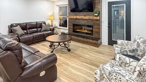 Ein Wohnzimmer mit Ledersofa, einem gemusterten Sessel, einem Flachbildfernseher, einem Kamin und einem Deckenventilator.