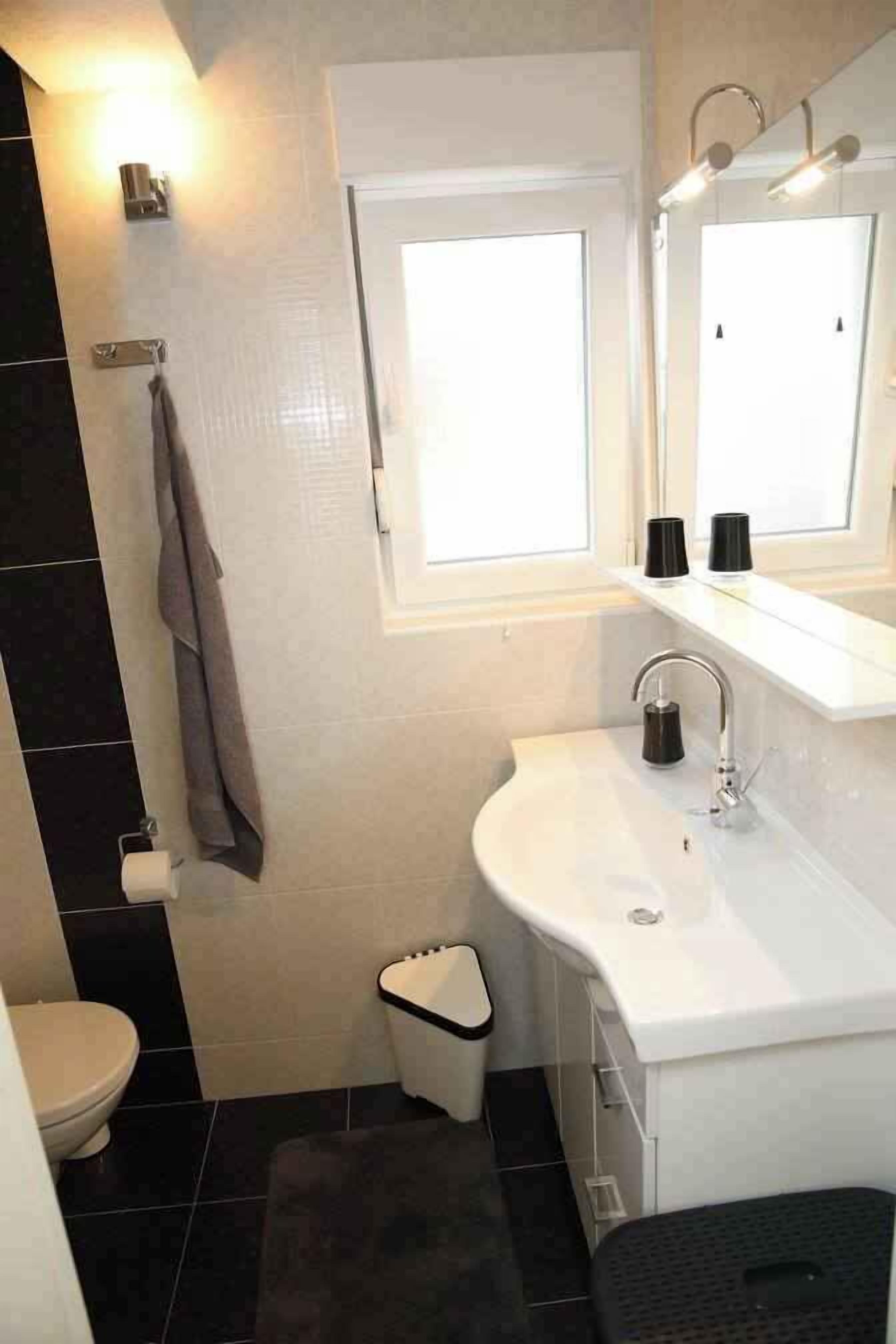 Un baño con lavamanos blanco, un espejo, toallero y una ventana.