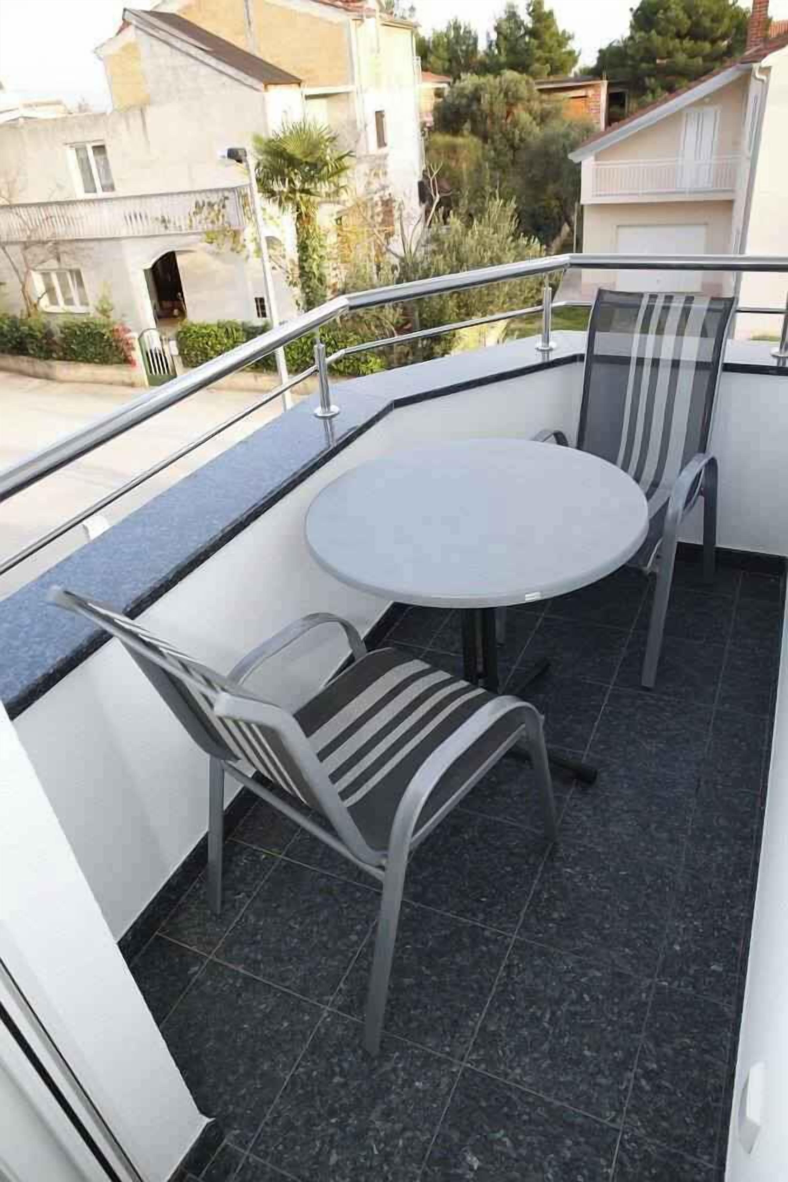 A balcony with a round table and two chairs, a metal railing, and a view of neighboring houses.